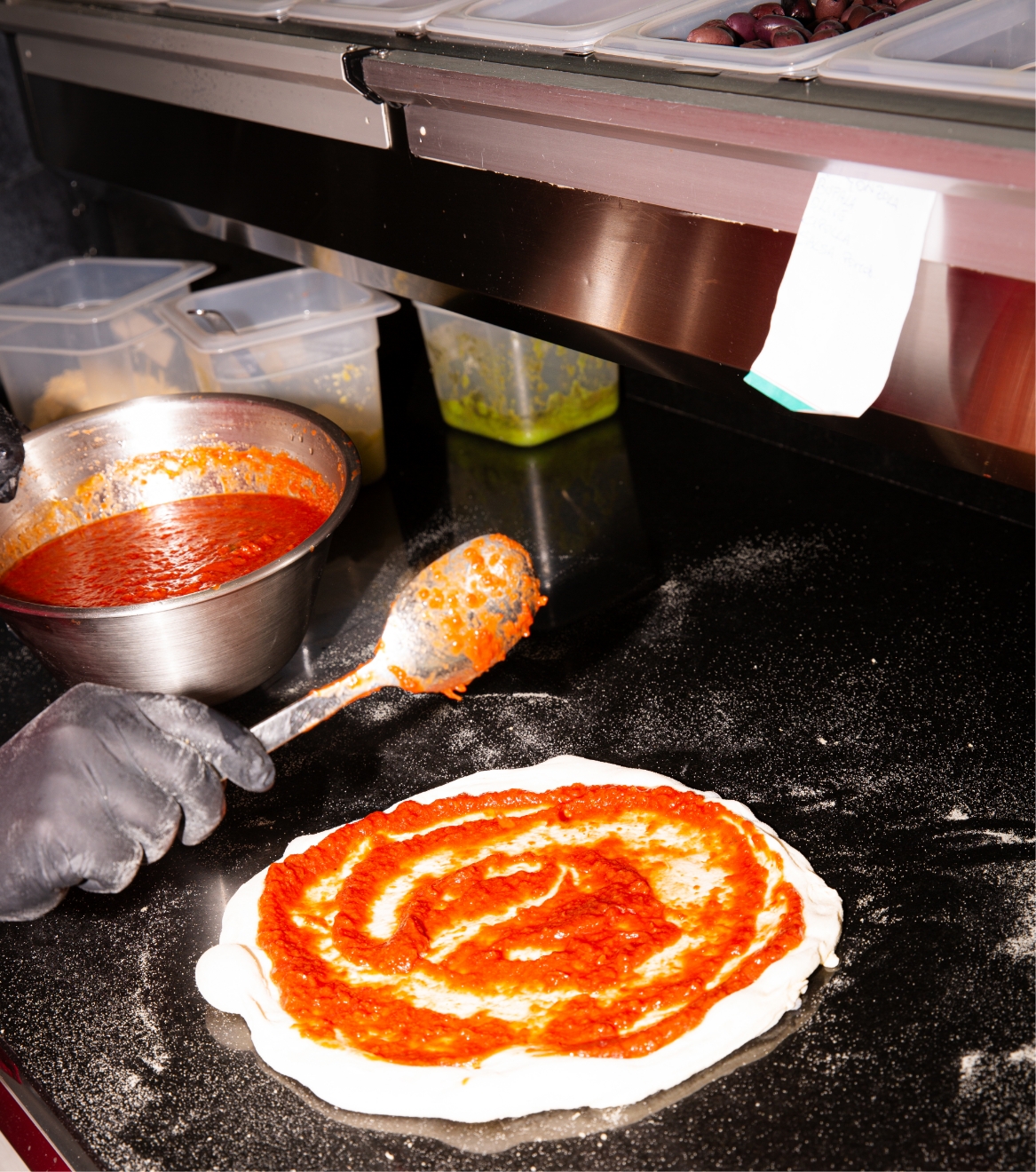 Zubereitung einer Pizza: Tomatensauce auf dem Teigboden