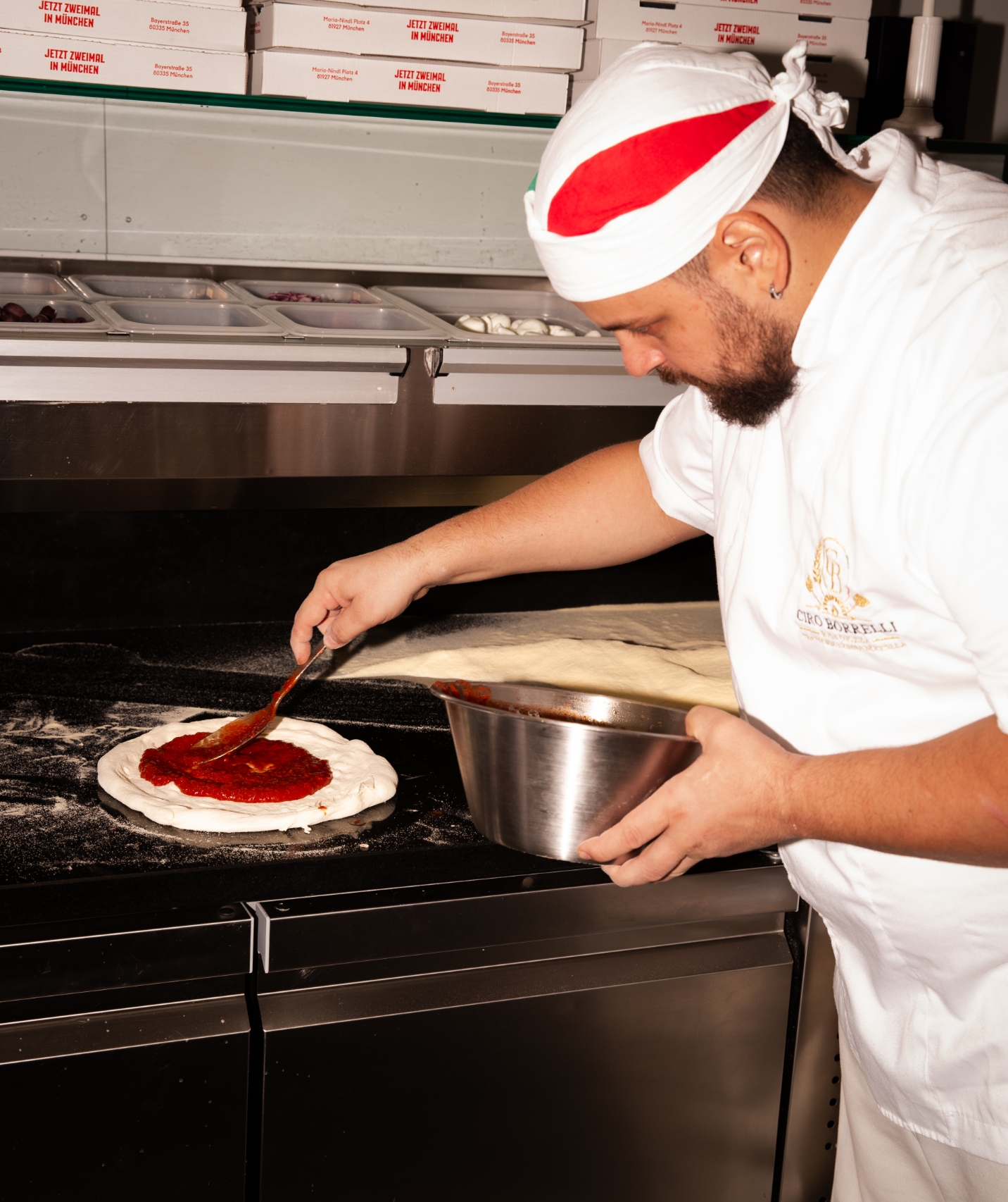 Pizzaiolo streicht Tomatensauce auf den Pizzateig
