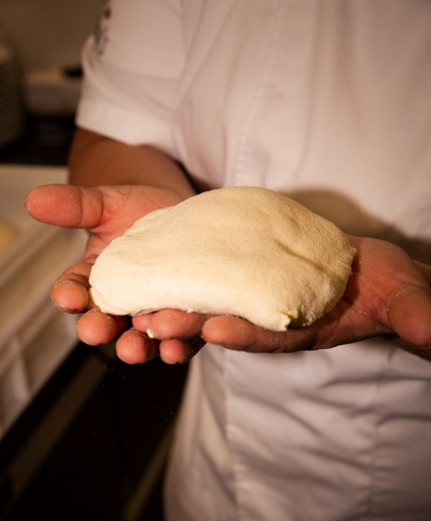 Hände halten einen handgemachten Pizzateig